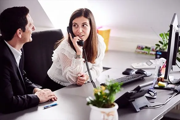 Zwei Mitarbeitende am Schreibtisch, eine telefoniert